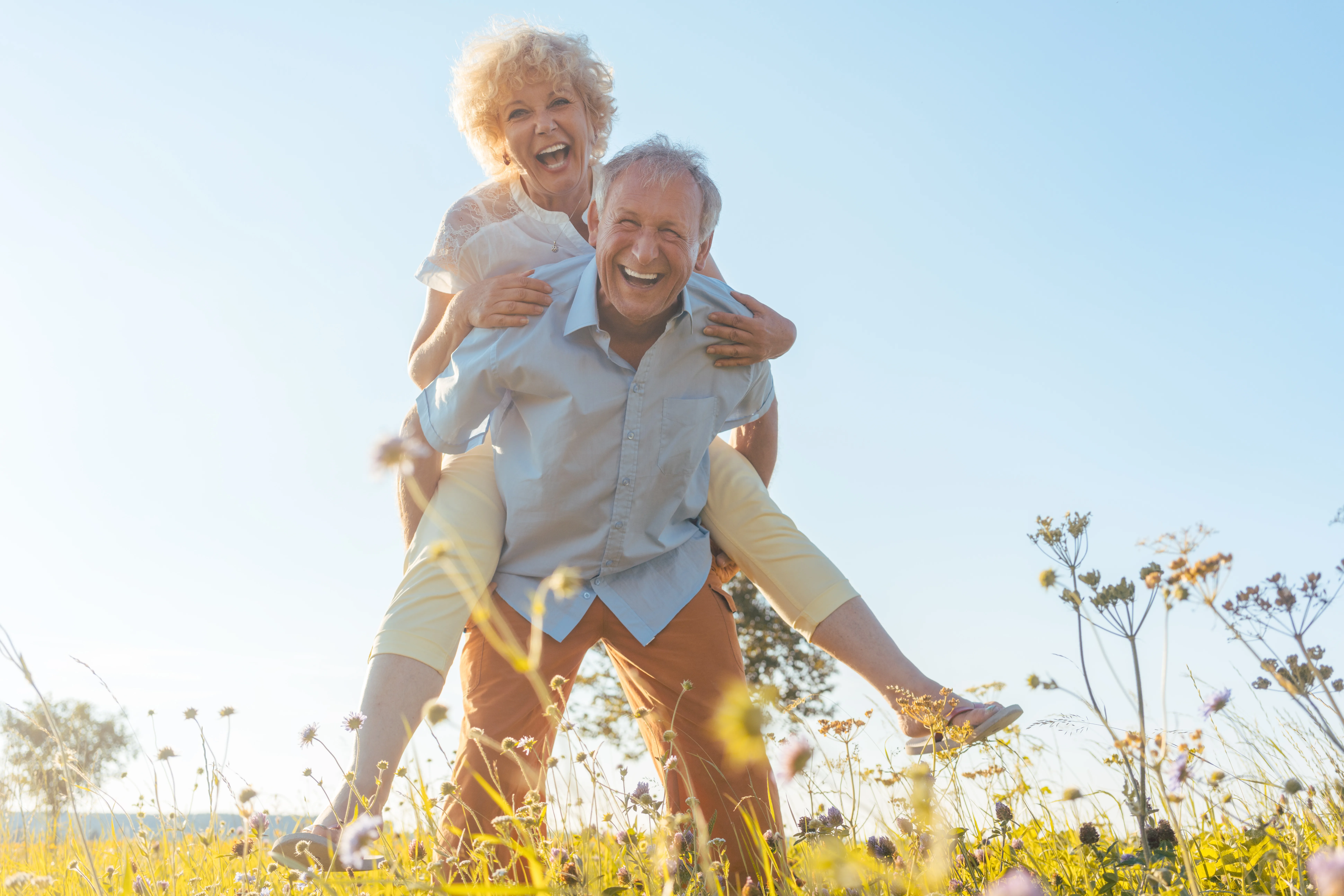 Happy senior man laughing while carrying his partner on his back in the countryside Low-angle view portrait of a happy senior man laughing while carrying his partner on his back in a sunny day of summer in the countryside