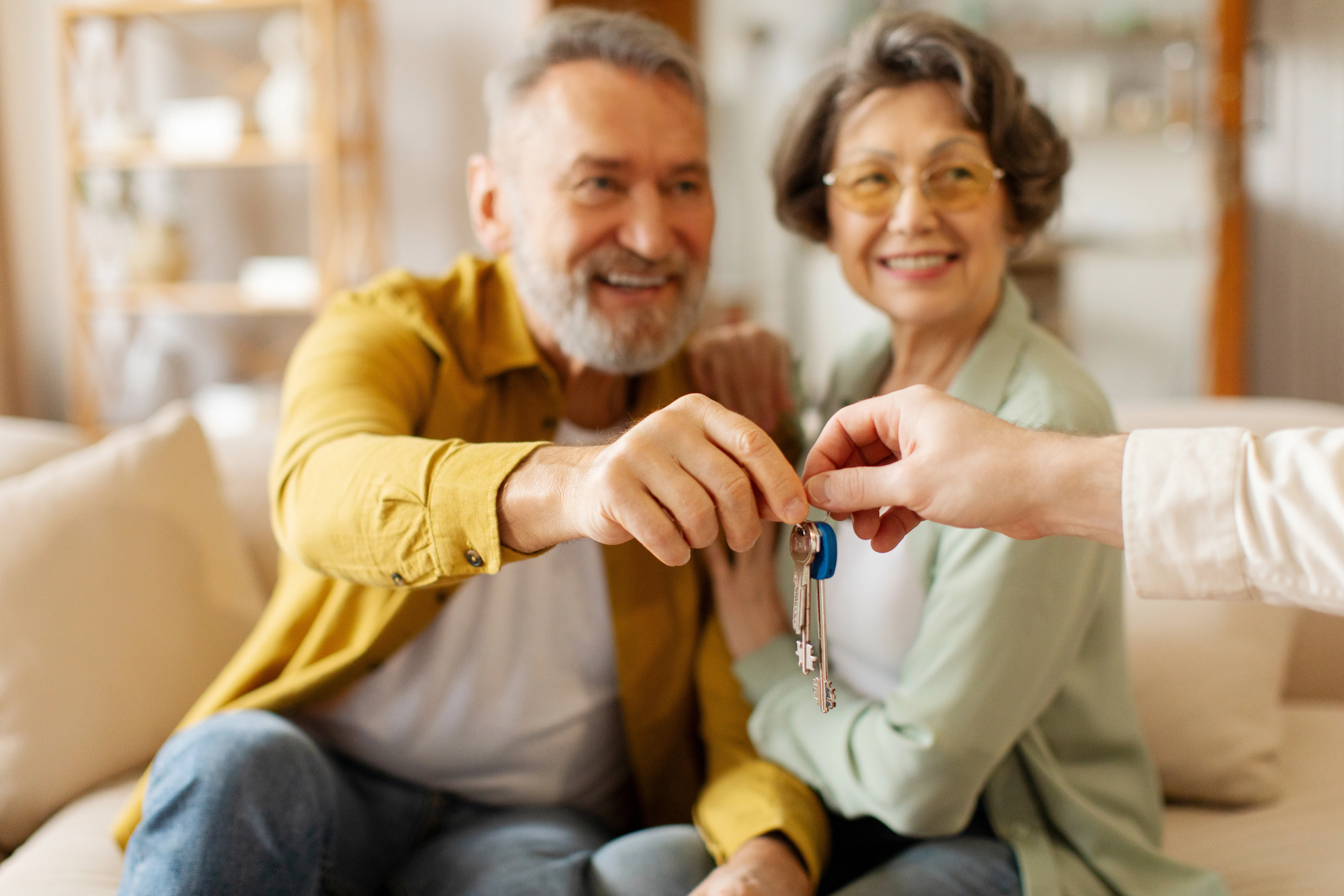 Retired couple buy house. Senior spouses become homeowners receiving key from new home in realtor office after closing deal