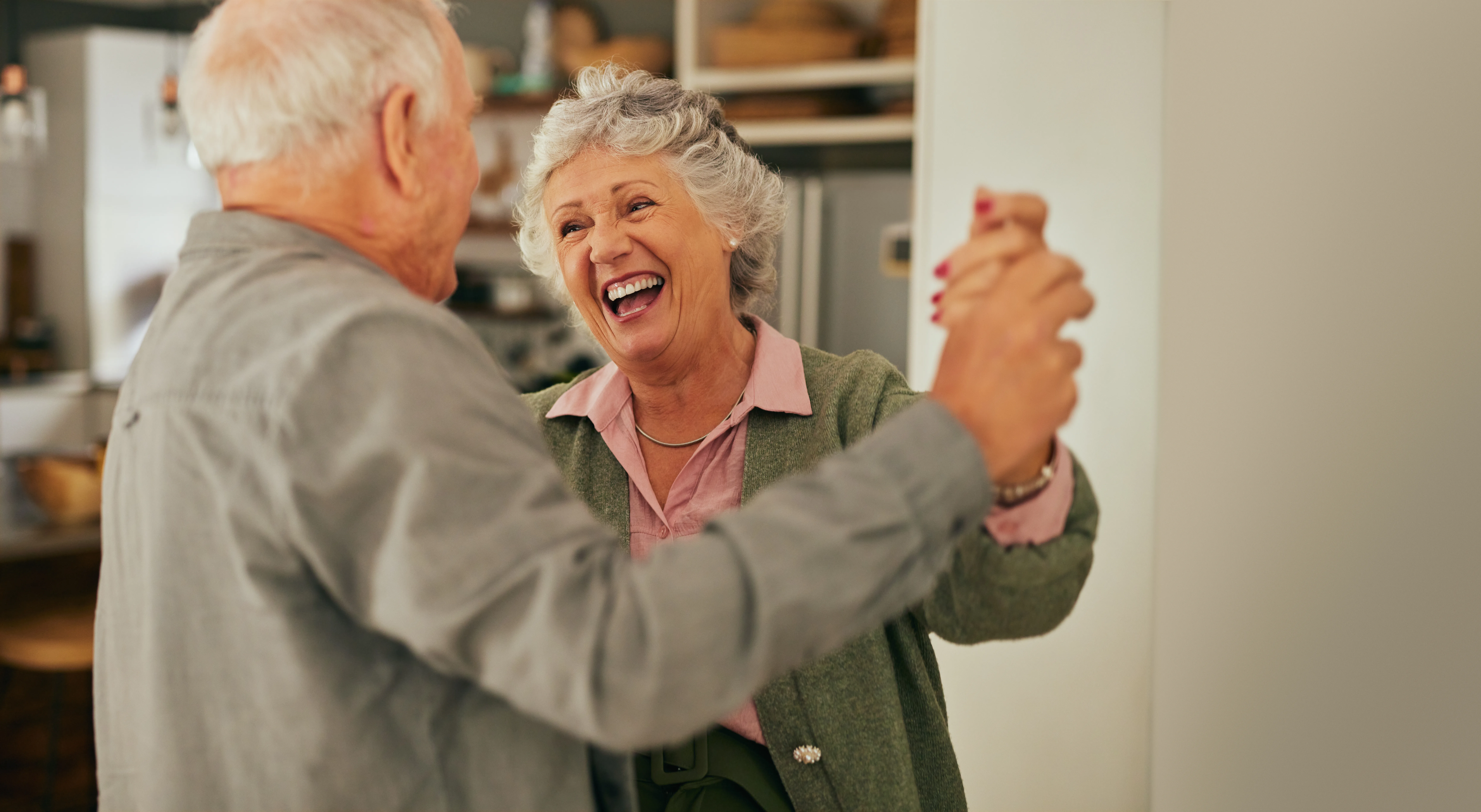 Elderly couple laughing joyfully while dancing together at home. Happy senior couple enjoying a dance in their living room. Mature woman expressing love and connection while dancing with her husband at home with copy space