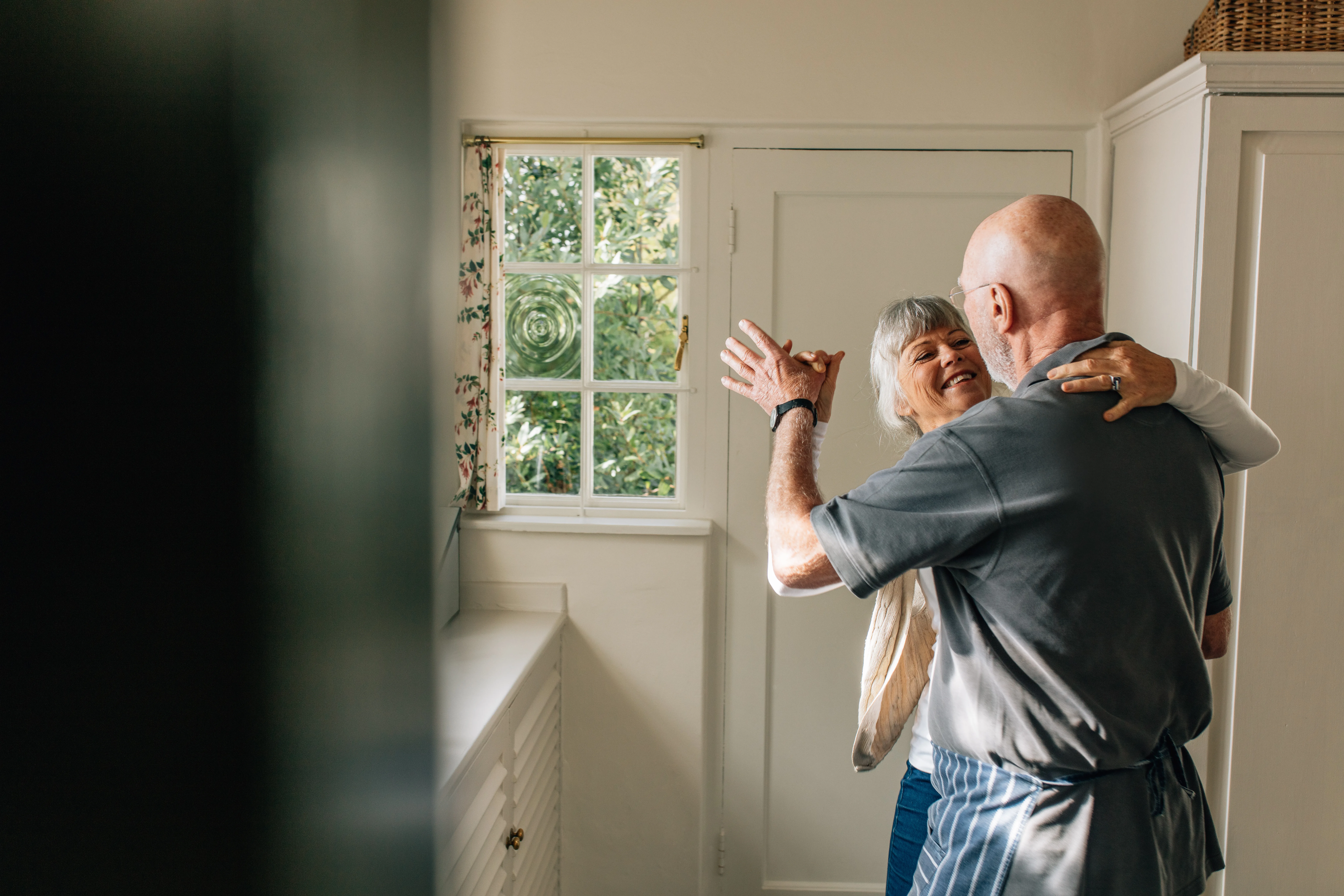 Happy elderly couple dancing together holding each other. Romantic senior couple having fun doing ballroom dancing at home.