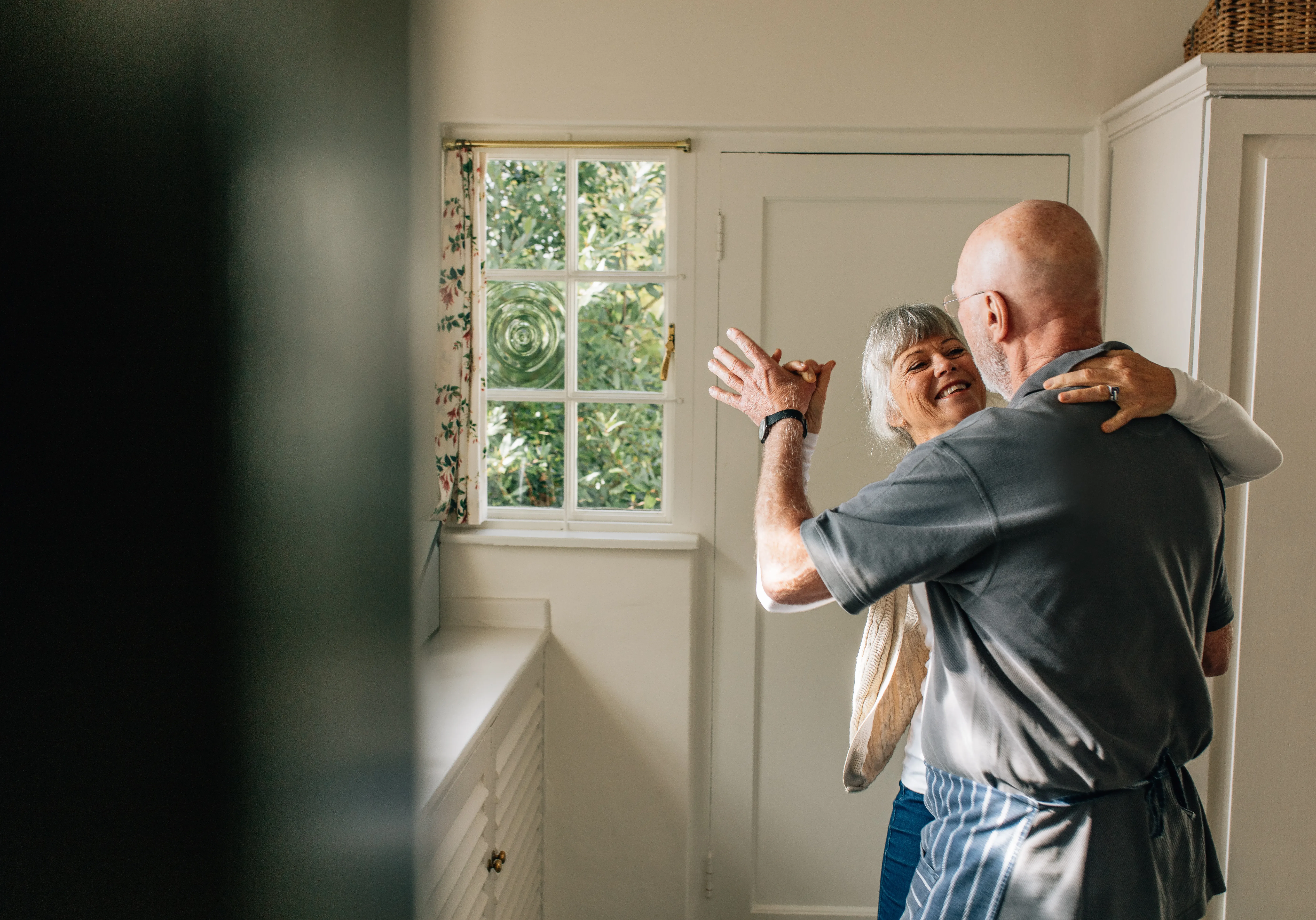 Happy elderly couple dancing together holding each other. Romantic senior couple having fun doing ballroom dancing at home.